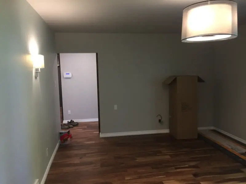 empty-room-with-light-fixtures A minimalistic room with wooden flooring, a wall-mounted light fixture, and a large ceiling lamp. Theres an open doorway leading to another room. A cardboard box and some items are on the floor near the doorway.