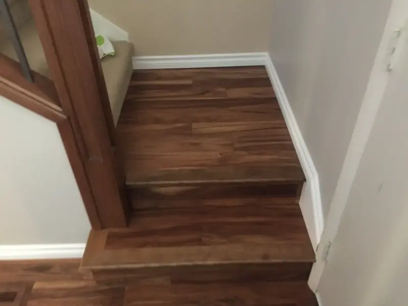 hardwood-staircase-corner A small set of wooden stairs with two steps, leading to a higher level in a house. The stairs are surrounded by a white wall and a wooden railing on the left side.