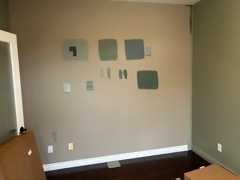 wall-with-paint-samples Wall with various gray and green paint swatches, each in different shapes and sizes. A door is partially visible on the left, and a wooden floorboard runs along the bottom.