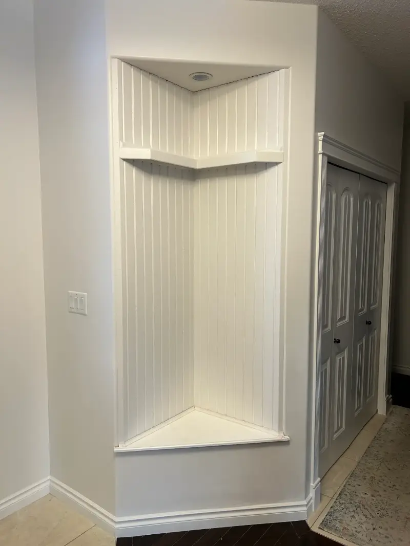 white-corner-display-niche Corner built-in white recessed shelf with beadboard backing and a spotlight above.